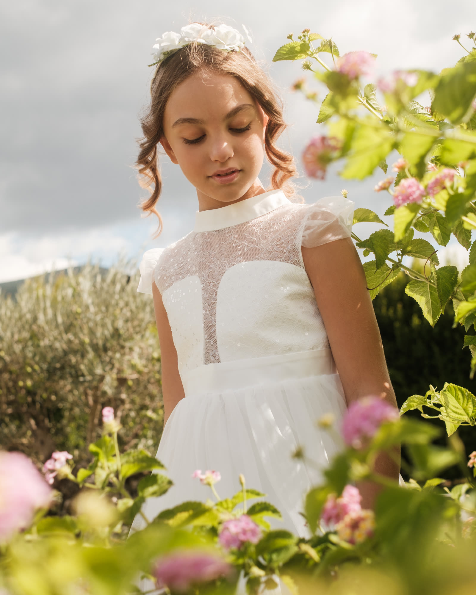Bambina con abito da cerimonia in pizzo bianco Illiana tra i fiori del giardino